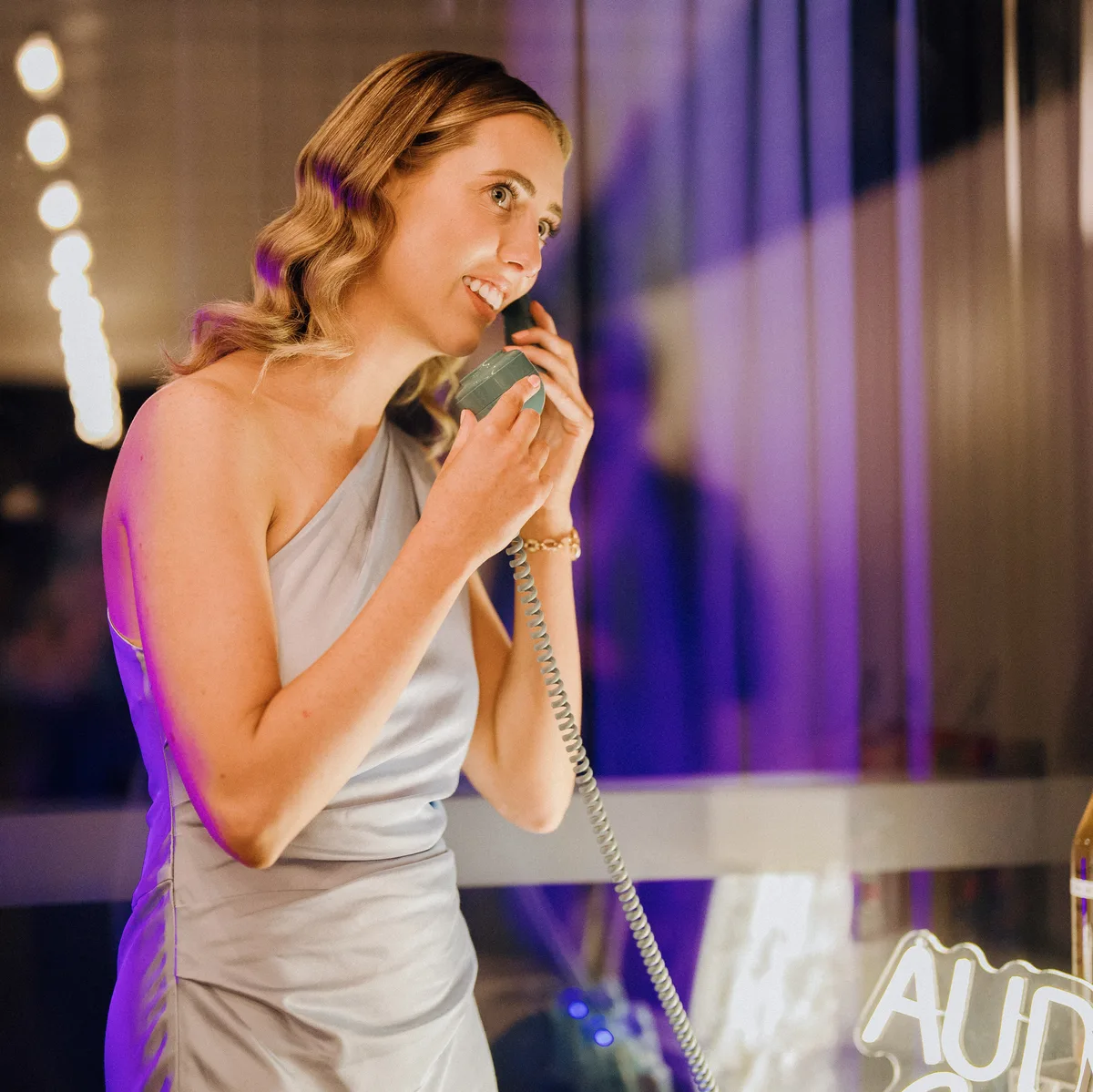 A wedding guest smiling as she listens on a mint Loveline phone