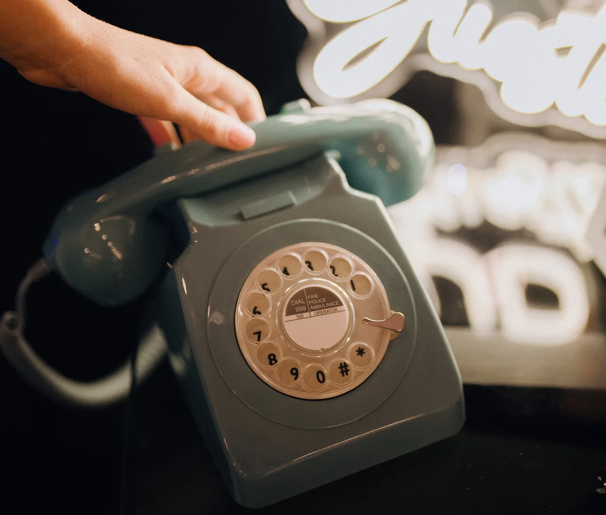 A guest lifting the handset of a sky blue Loveline phone under a neon audio guestbook sign